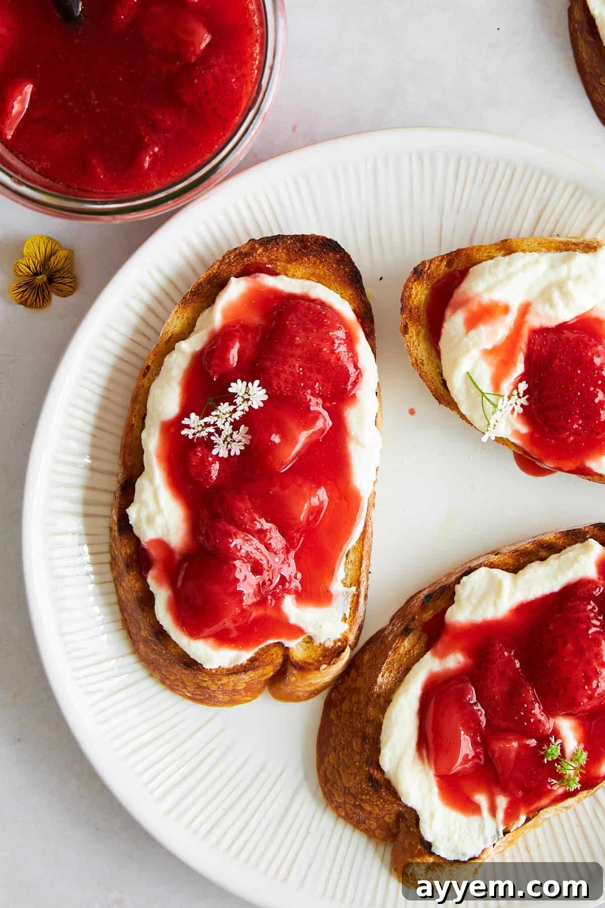 Close-up of two pieces of strawberry ricotta toast on a plate, highlighting the rich toppings.