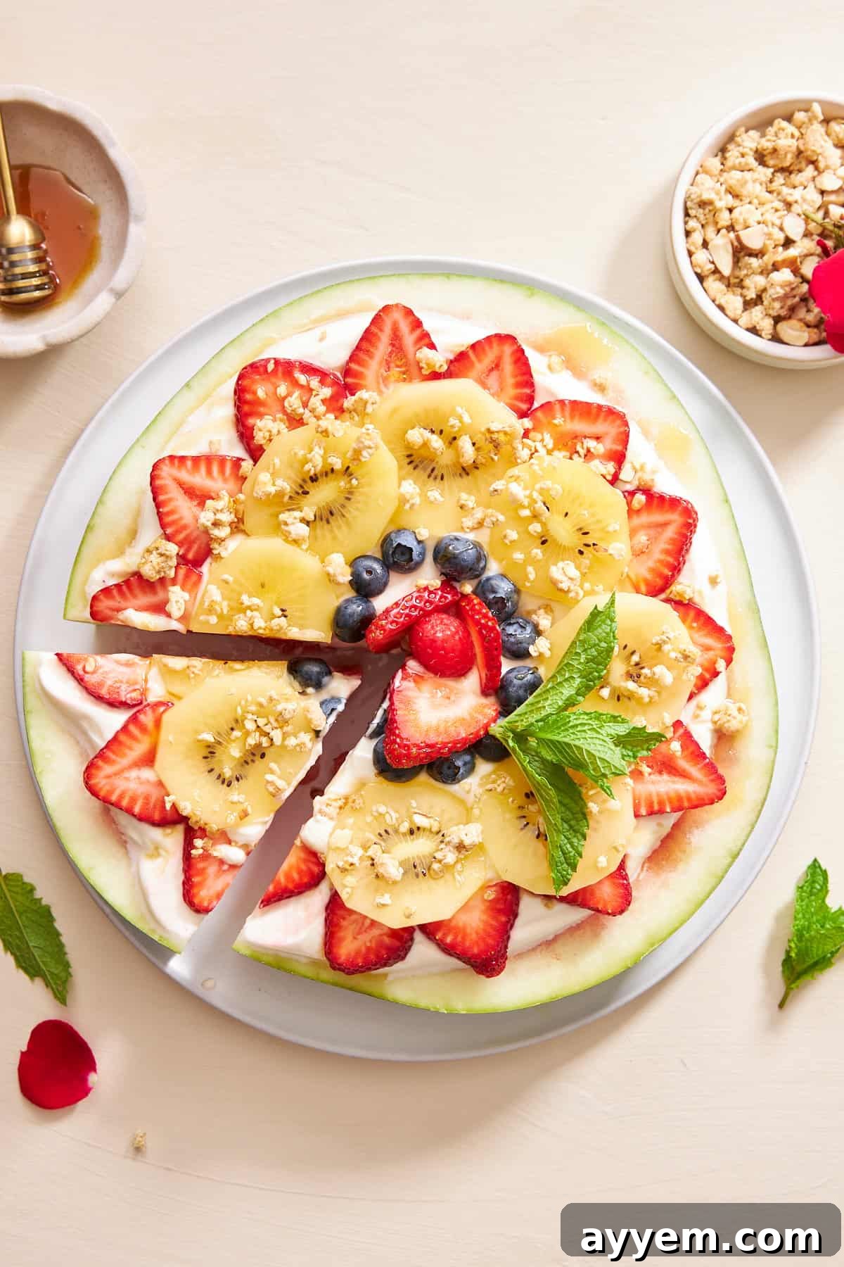 A beautifully garnished watermelon pizza with one slice already cut, showcasing vibrant fruits and creamy topping.