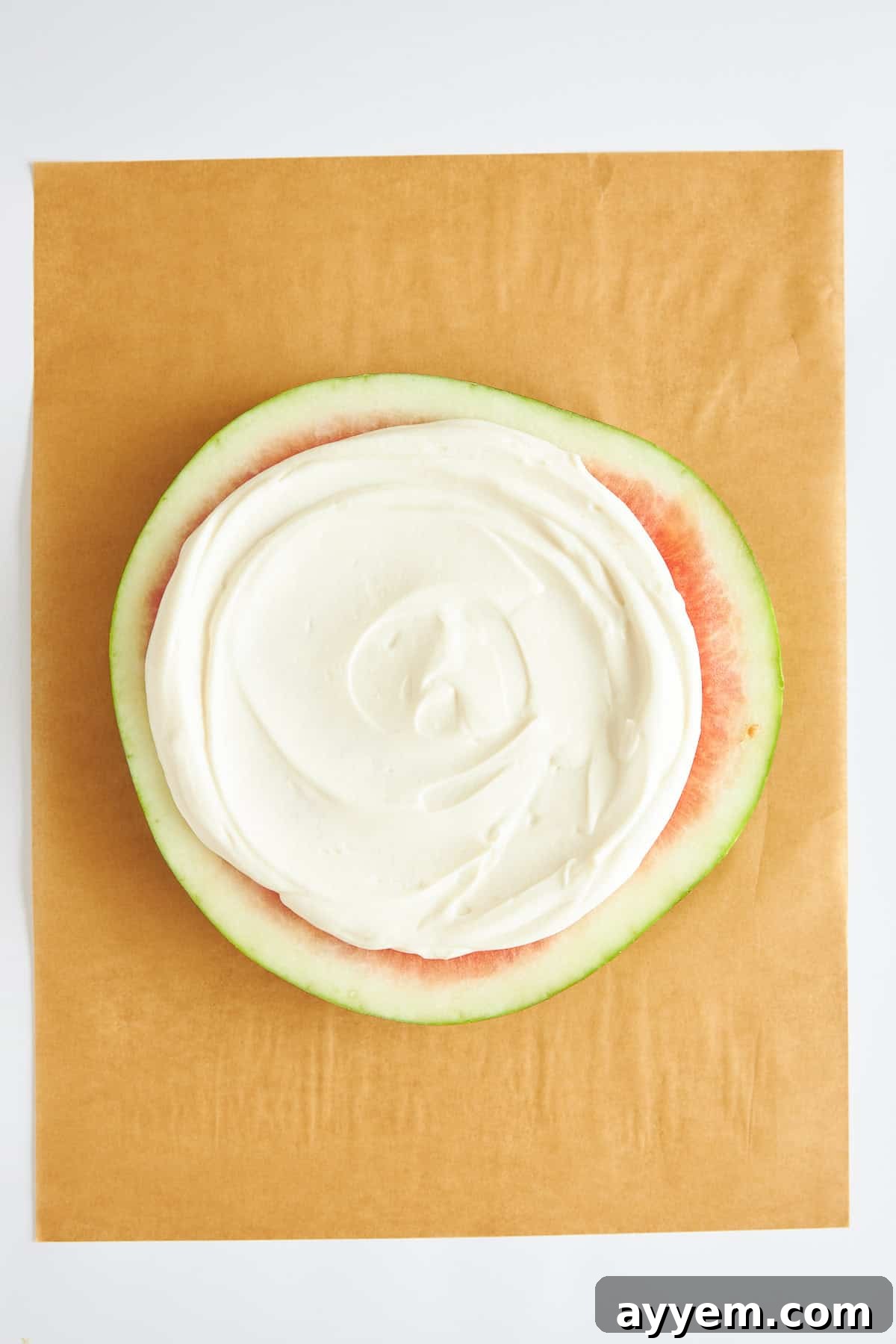 A round watermelon slice evenly topped with a smooth layer of creamy Greek yogurt, resembling pizza sauce.