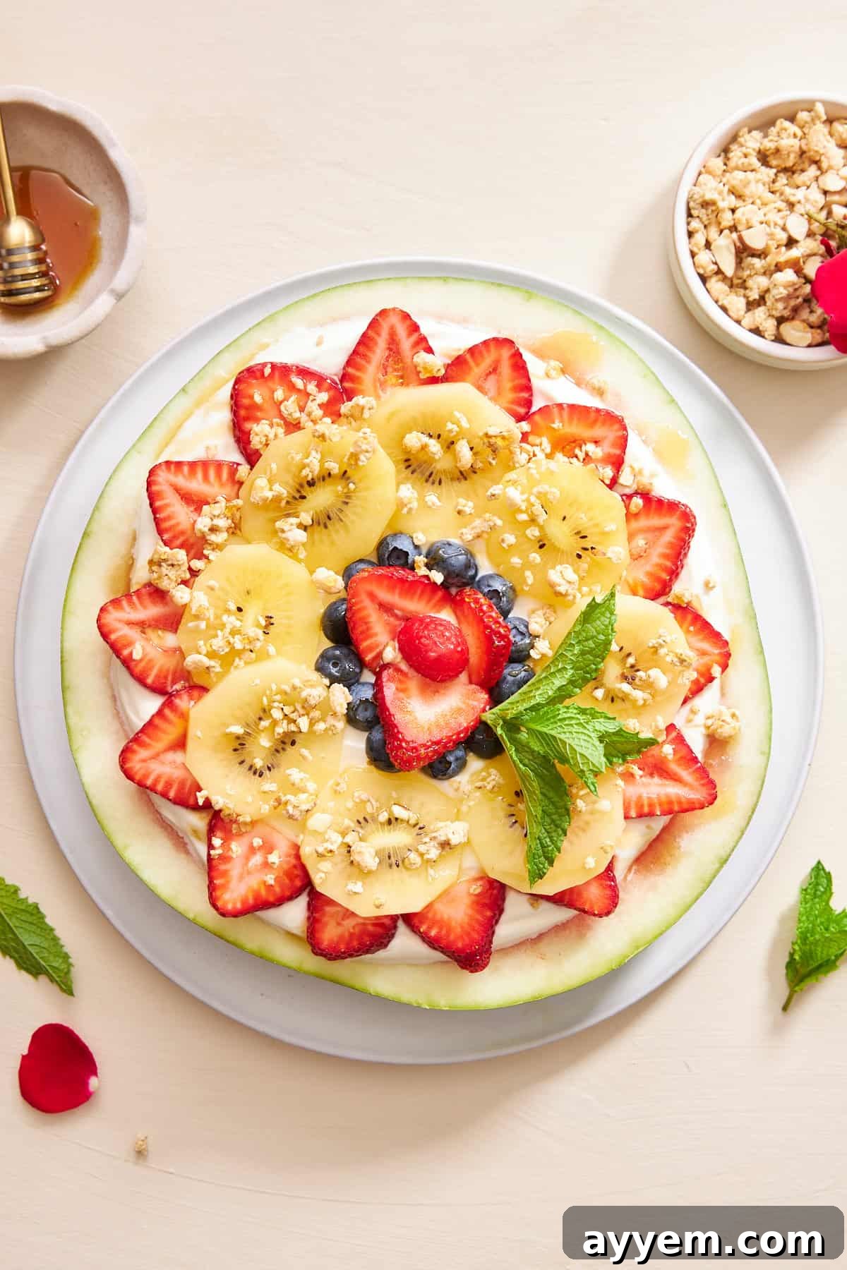 A fully prepared watermelon pizza, garnished with crunchy granola and fresh mint leaves, ready to be sliced and served.