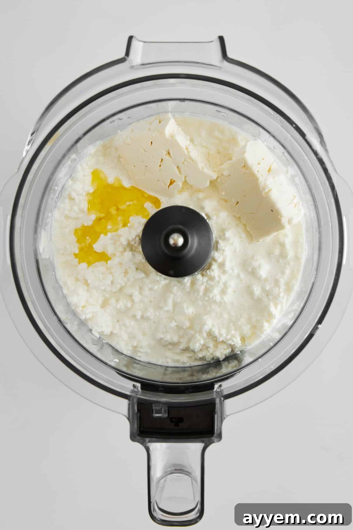 Cottage cheese, crumbled feta, and a drizzle of olive oil waiting to be blended in a food processor, capturing the initial stage of creating the creamy base.