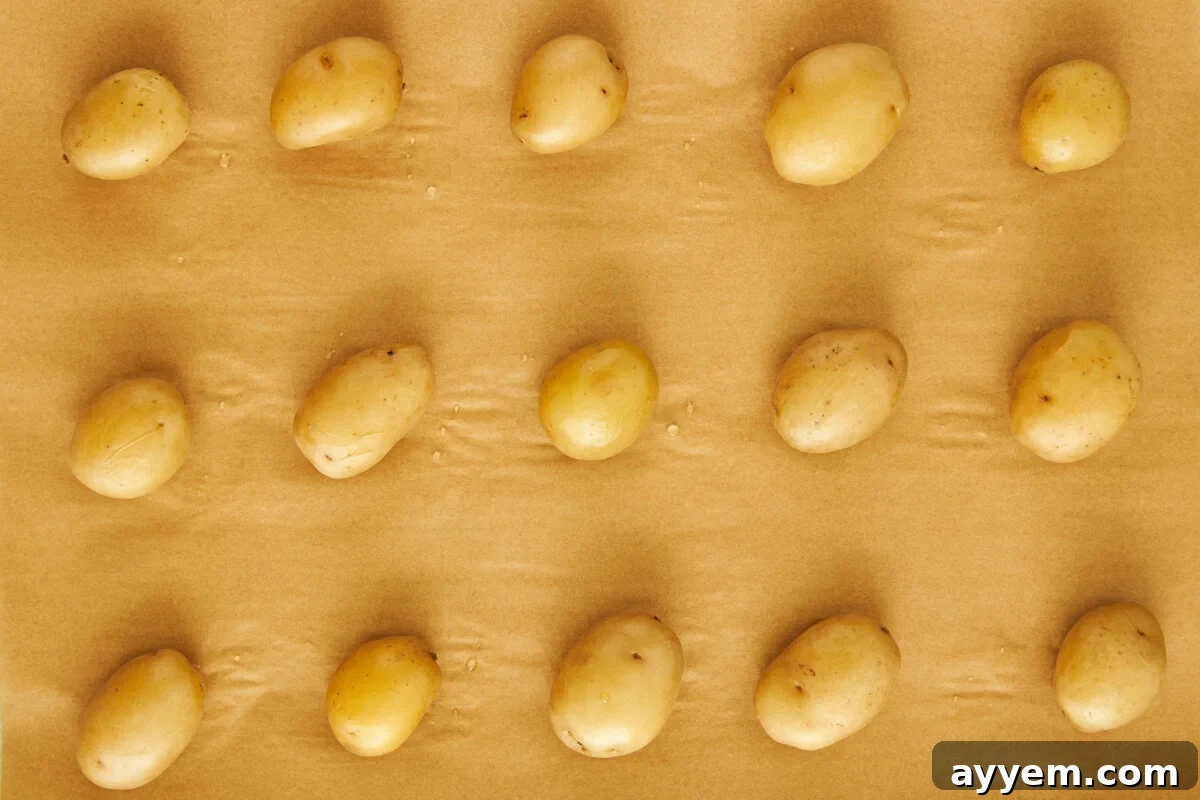 Boiled potatoes on a parchment paper-lined baking sheet.
