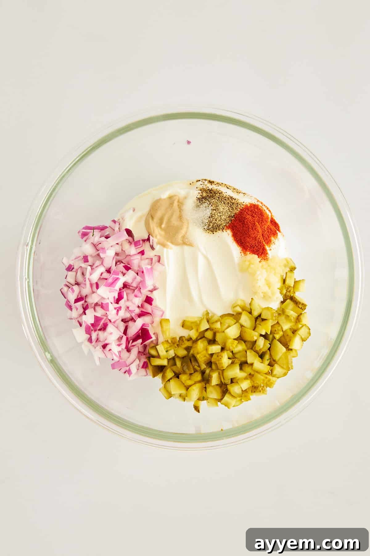 A bowl showcasing the vibrant components of the labneh dressing: creamy labneh, chopped pickles, diced red onion, and fresh seasonings, ready to be mixed.