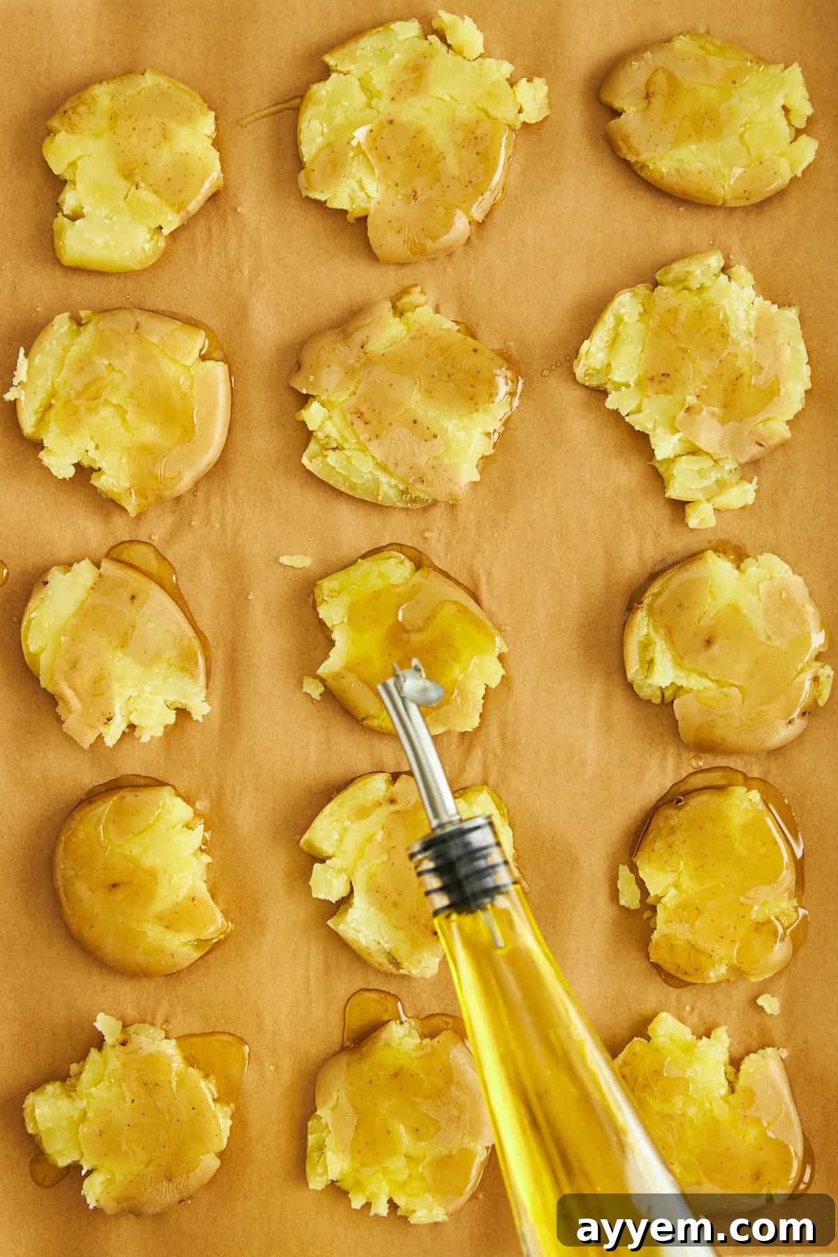Uncooked smashed potatoes on a parchment-lined baking sheet, generously drizzled with olive oil, illustrating the preparation for achieving maximum crispiness.