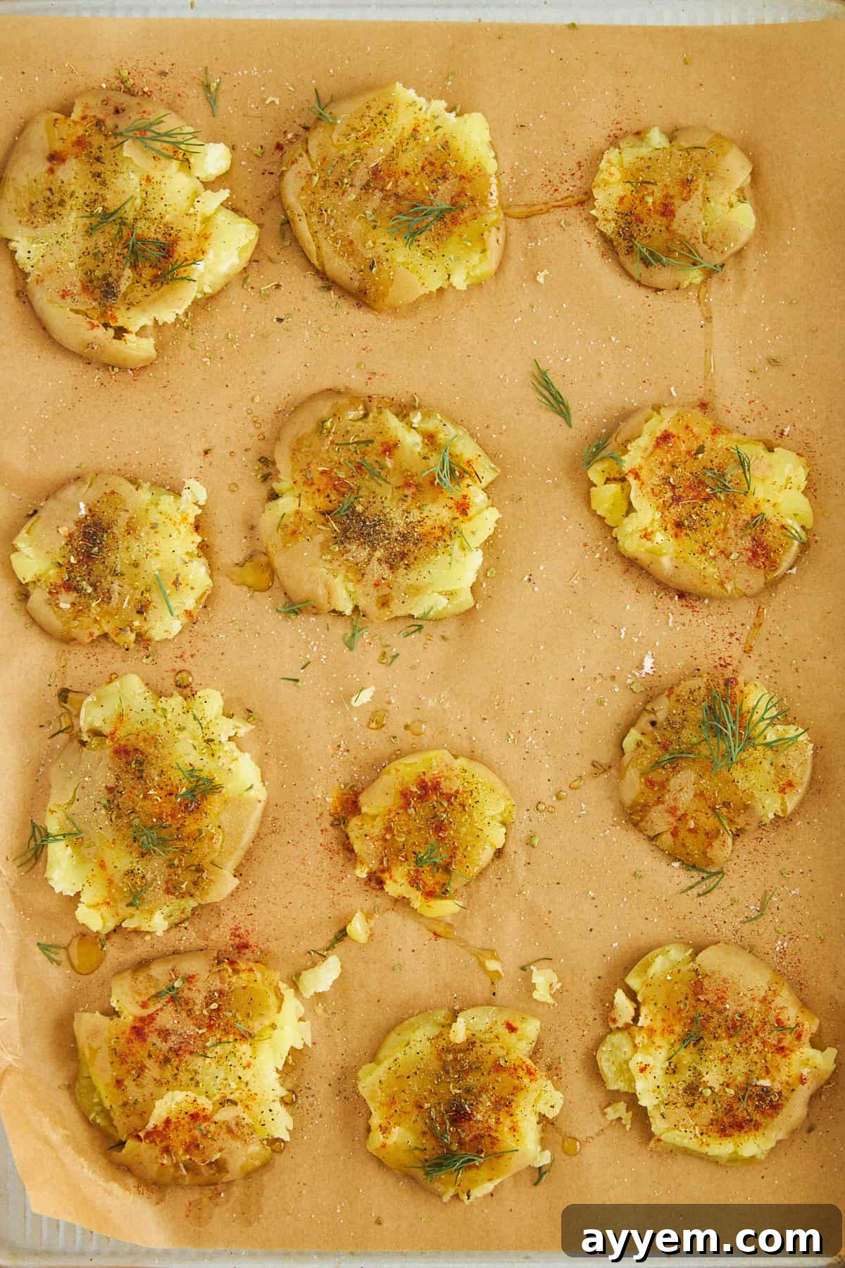 Uncooked smashed potatoes, beautifully seasoned with oil and spices, arranged on a baking sheet.