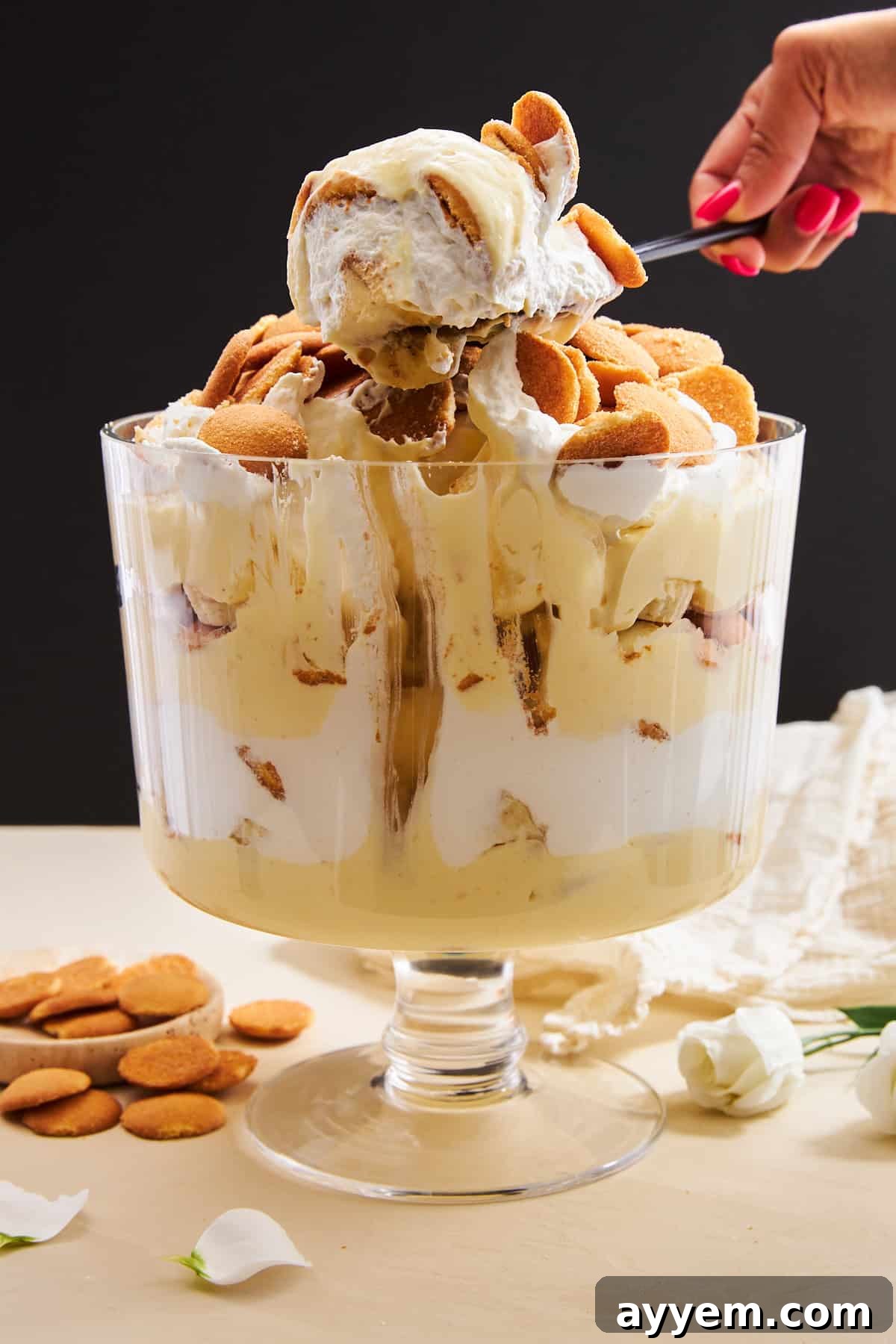 A serving spoon lifting a generous scoop of easy banana pudding from a decorative trifle bowl, showing the creamy layers.