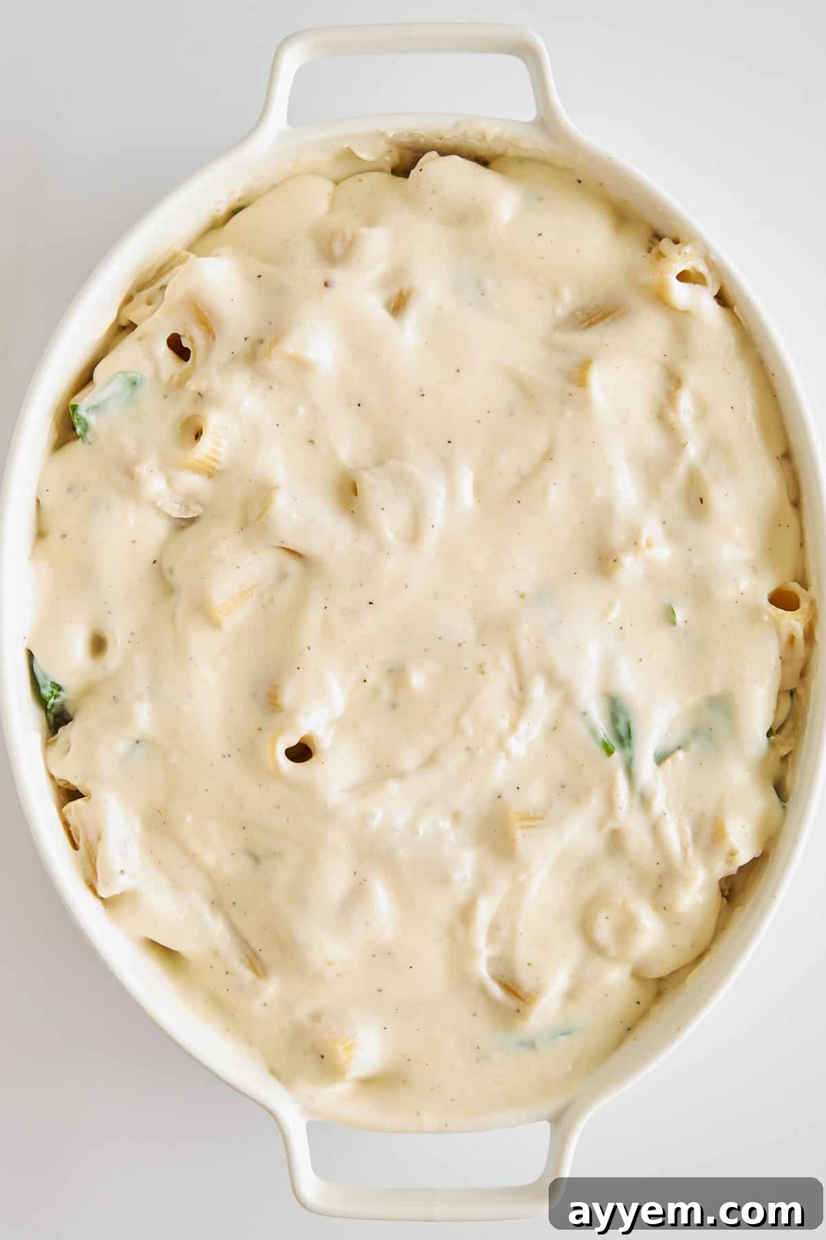 Uncooked Chicken Spinach Pasta Bake mixture, featuring pasta, chicken, and spinach evenly coated in a creamy sauce, before adding cheese.