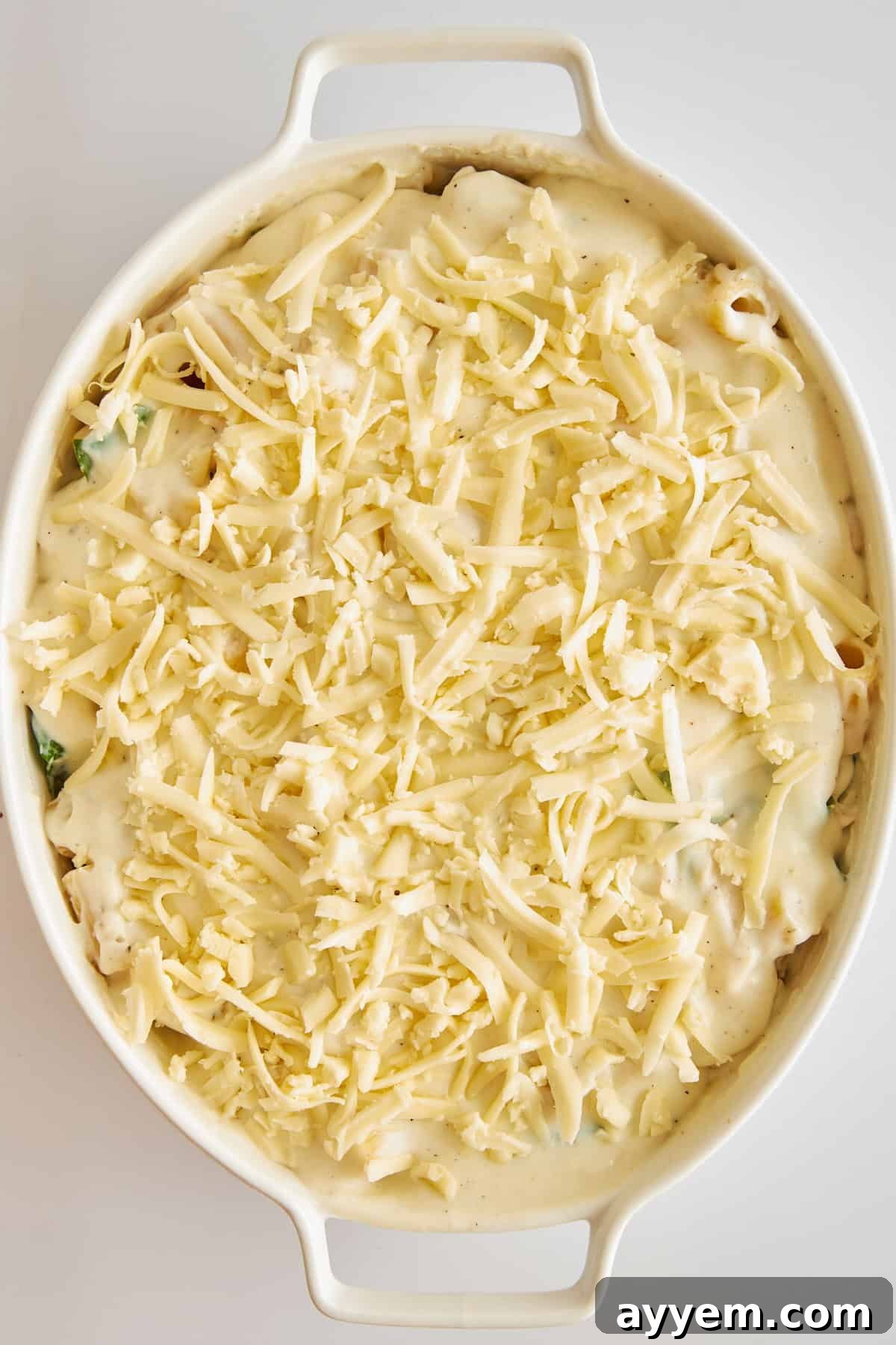 Uncooked Chicken Spinach Pasta Bake in a baking dish, generously topped with shredded Fontina cheese, ready for baking.