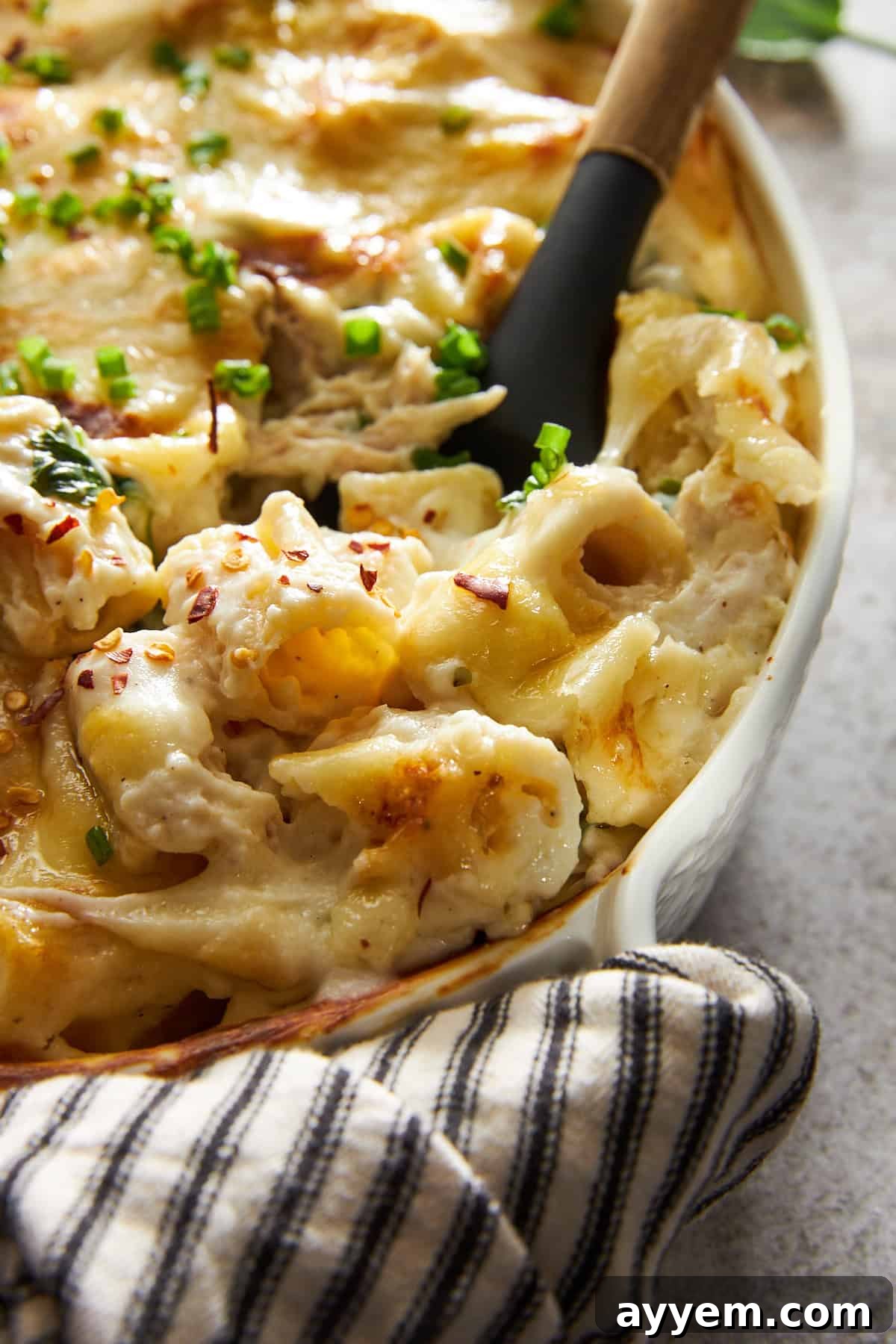 Close up view of a serving of chicken spinach pasta bake with a spoon sunk in, showing the rich sauce, tender chicken, and melted cheese.