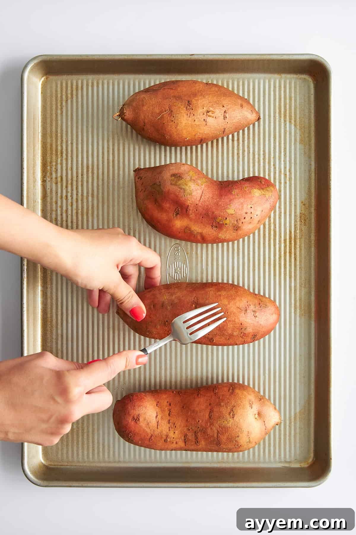 Creamy Dairy-Free Sweet Potato Mash 3 Four sweet potatoes on a baking sheet being pricked with forks.
