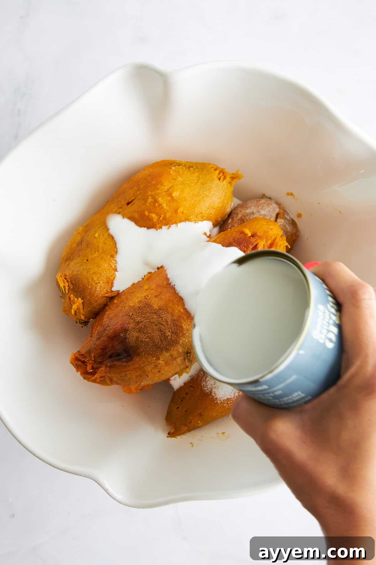 Creamy Dairy-Free Sweet Potato Mash 5 Coconut milk being poured over baked sweet potatoes in a bowl.