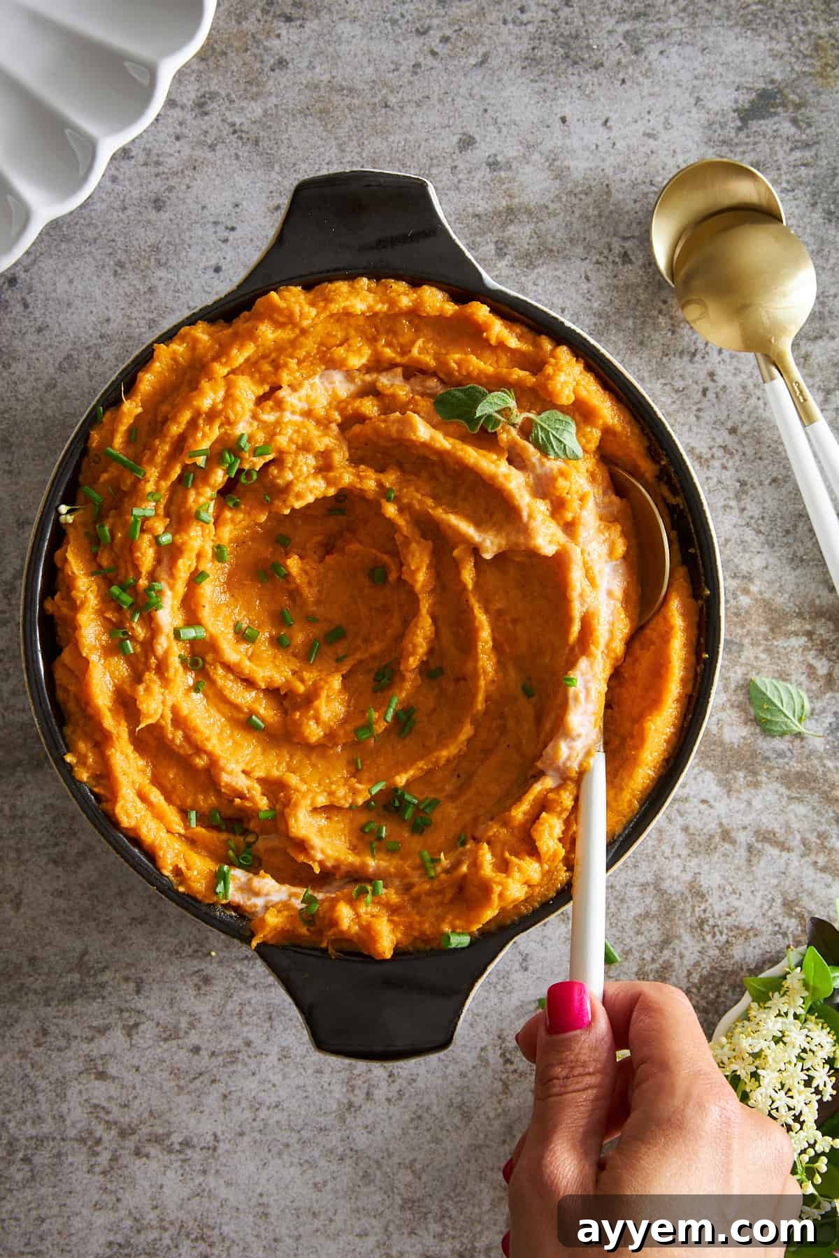 A hand holding a spoon in a bowl of dairy free mashed sweet potatoes.