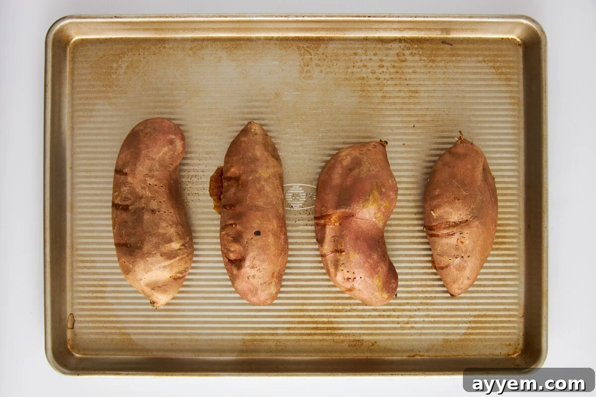 Four sweet potatoes on a baking sheet.
