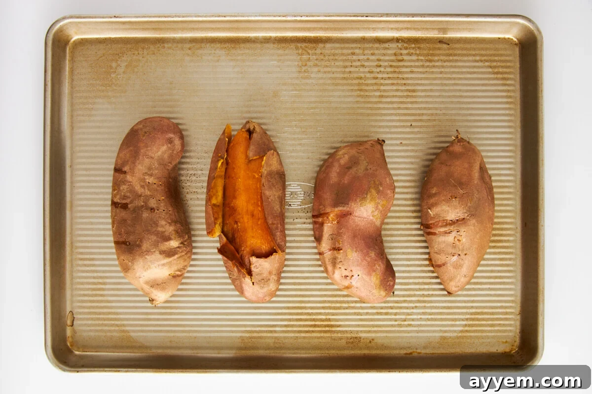 Four roasted sweet potatoes on a baking sheet.