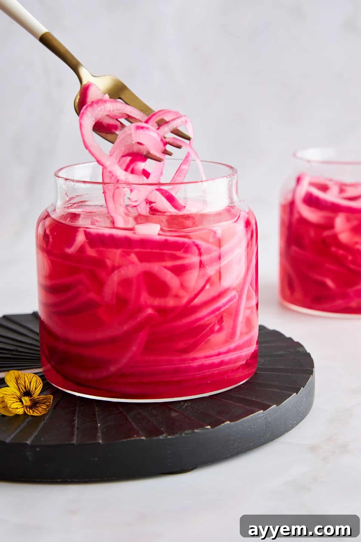 A fork lifting pickled red onions from a jar. 