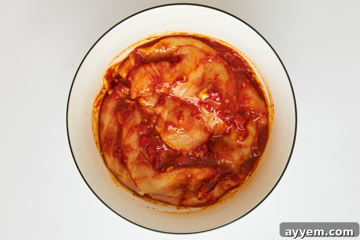 Chicken marinading in honey harissa sauce, showing the rich red color.