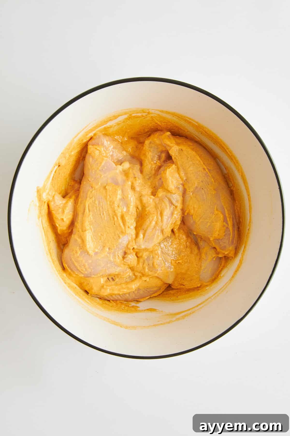 Raw chicken in a bowl with hummus marinade, thoroughly coated.