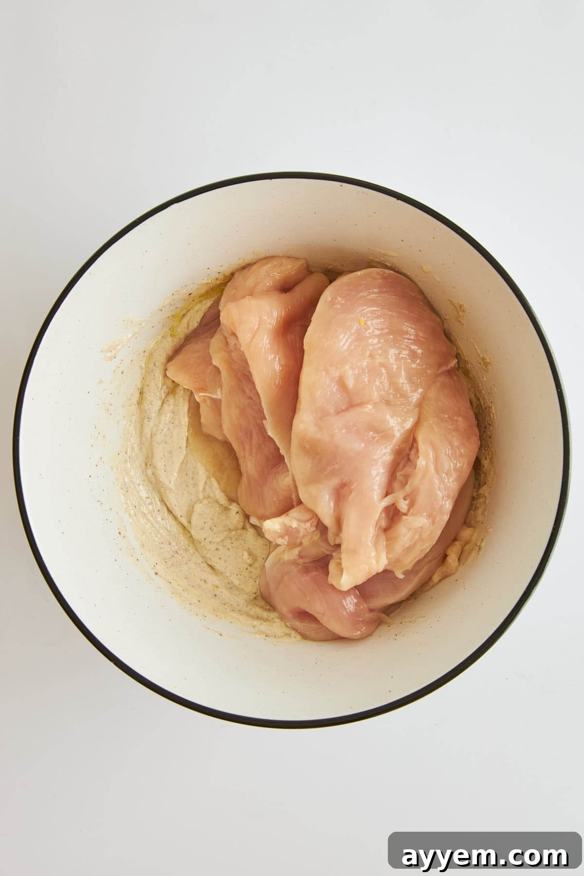 Raw chicken and tahini yogurt marinade in a bowl, ready to be combined.