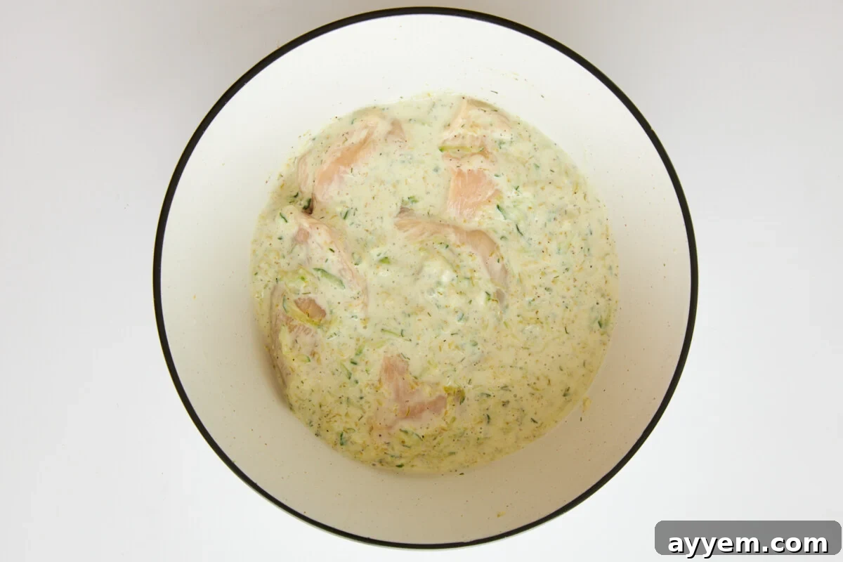 Chicken marinading in tzatziki sauce, showing the creamy texture coating the poultry.