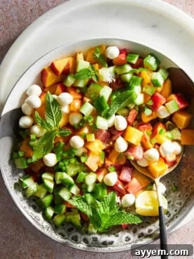 A colorful bowl of peach salad adorned with glistening mozzarella pearls, basil, and a balsamic glaze drizzle.