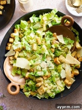 An overhead view of a classic Caesar salad, generously drizzled with creamy dressing and topped with crunchy croutons and Parmesan cheese.