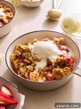 A bowl of strawberry crisp with a rich, golden oat topping, generously crowned with a scoop of vanilla ice cream, highlighting the vibrant red strawberries.