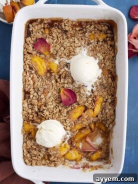 Overhead image of a baked peach crisp topped with two scoops of vanilla ice cream, with a serving removed from the bottom right, showcasing the sweet cinnamon sugar peaches and crumbly oat topping.
