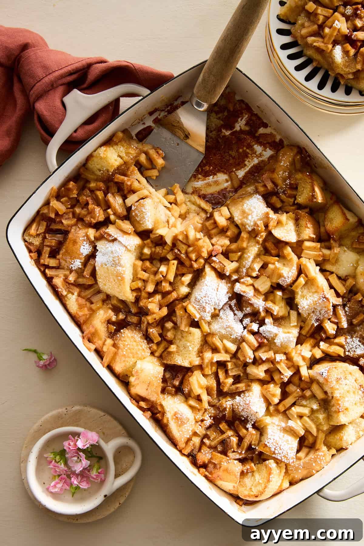 A serving dish of apple cinnamon french toast with a spatula in the spot of a missing serving. 
