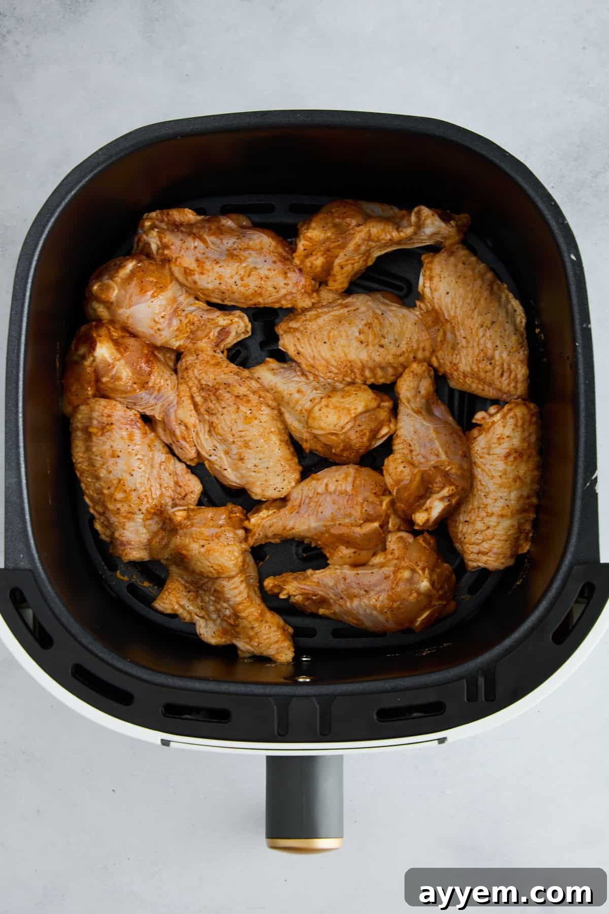 Raw seasoned chicken wings arranged in a single layer in an air fryer basket, ready for cooking.