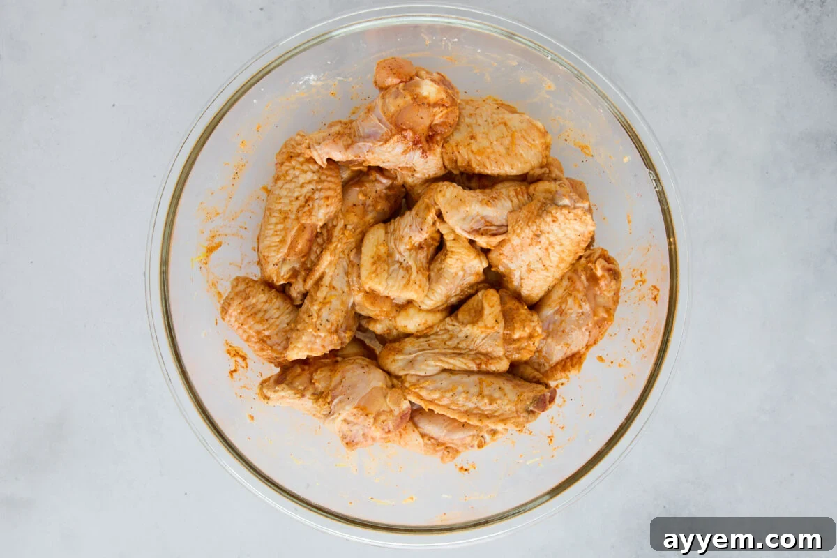 Raw chicken wings in a bowl tossed with seasonings.