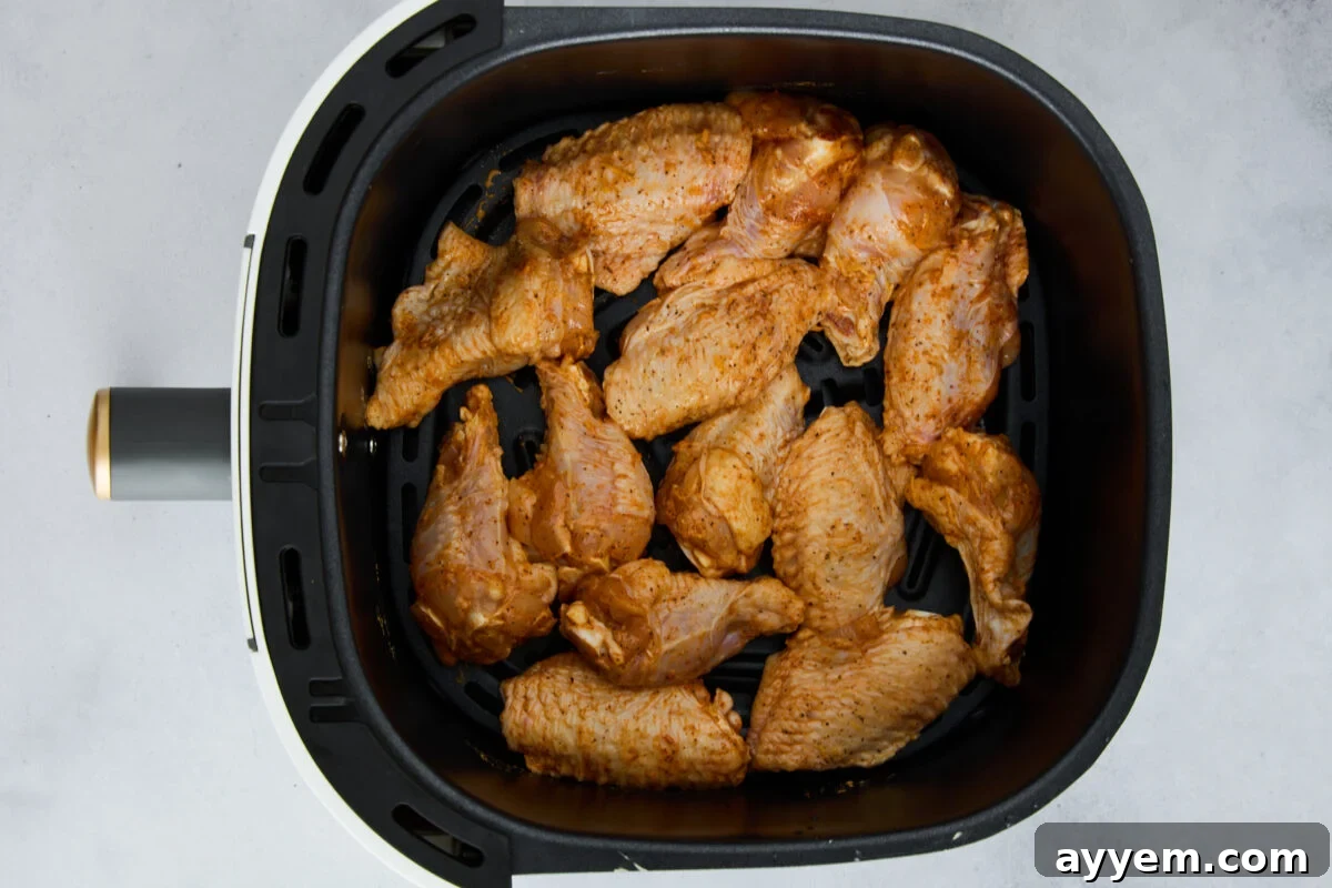 Raw chicken wings in an air fryer basket.