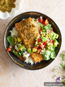 A vibrant bowl featuring baked salmon seasoned with Za'atar, served alongside fluffy white rice and a fresh avocado salsa.