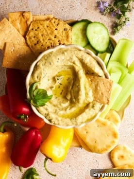 A beautifully presented bowl of creamy roasted zucchini dip, surrounded by an assortment of fresh vegetables like cucumbers, celery, mini bell peppers, pita bread, and crackers, perfect for dipping.