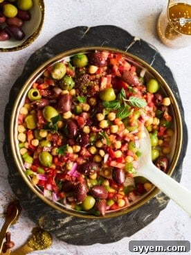 A vibrant and colorful bowl of Mediterranean olive salad, showcasing a medley of various olives, fresh vegetables, and aromatic herbs.