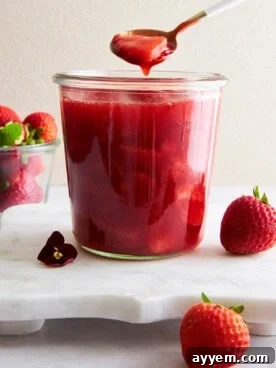 A spoon lifting a scoop of strawberry sauce from a jar.