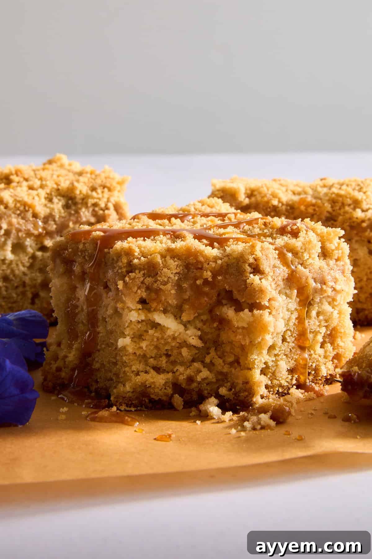 A slice of apple crumb cake topped with caramel sauce, showcasing its soft interior and generous crumb topping.