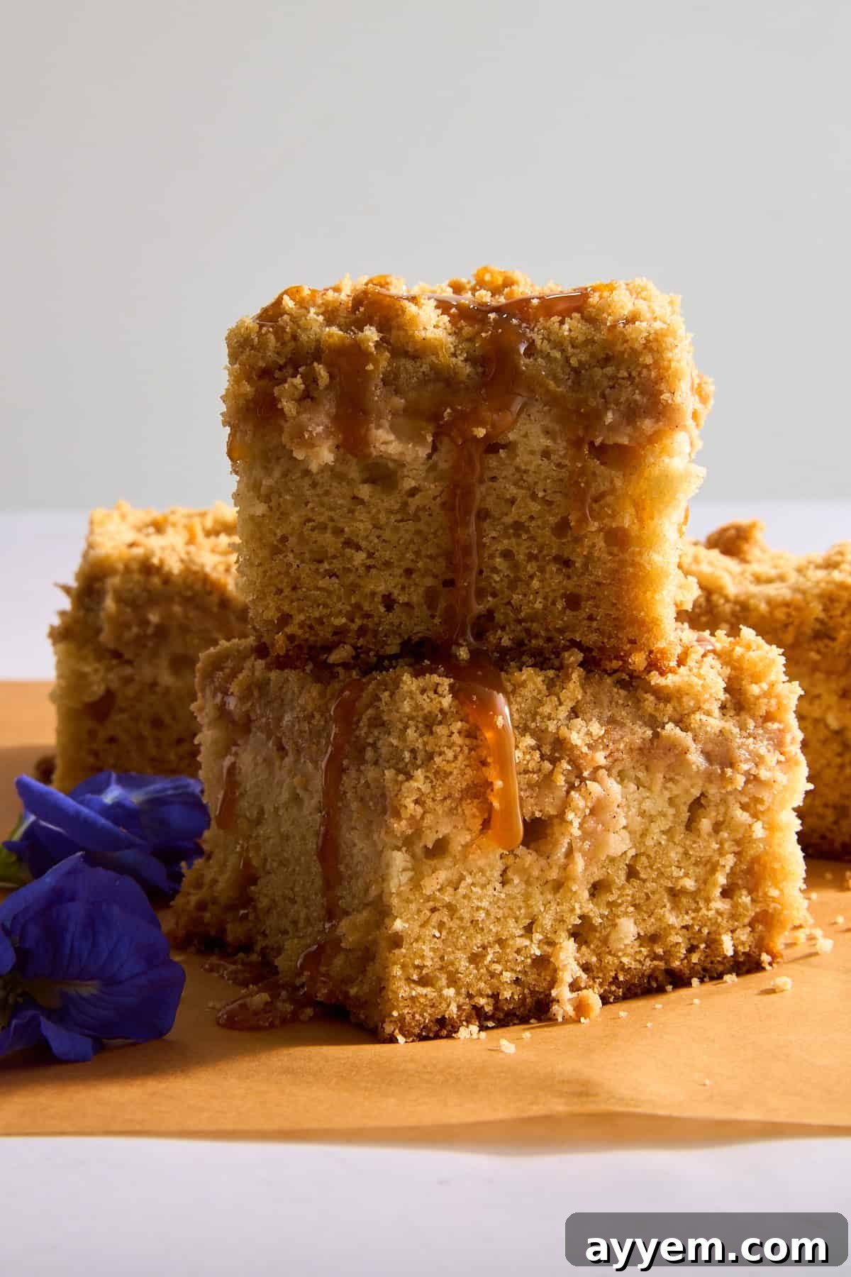 Two pieces of apple crumb cake stacked, drizzled with caramel sauce, highlighting the rich texture.