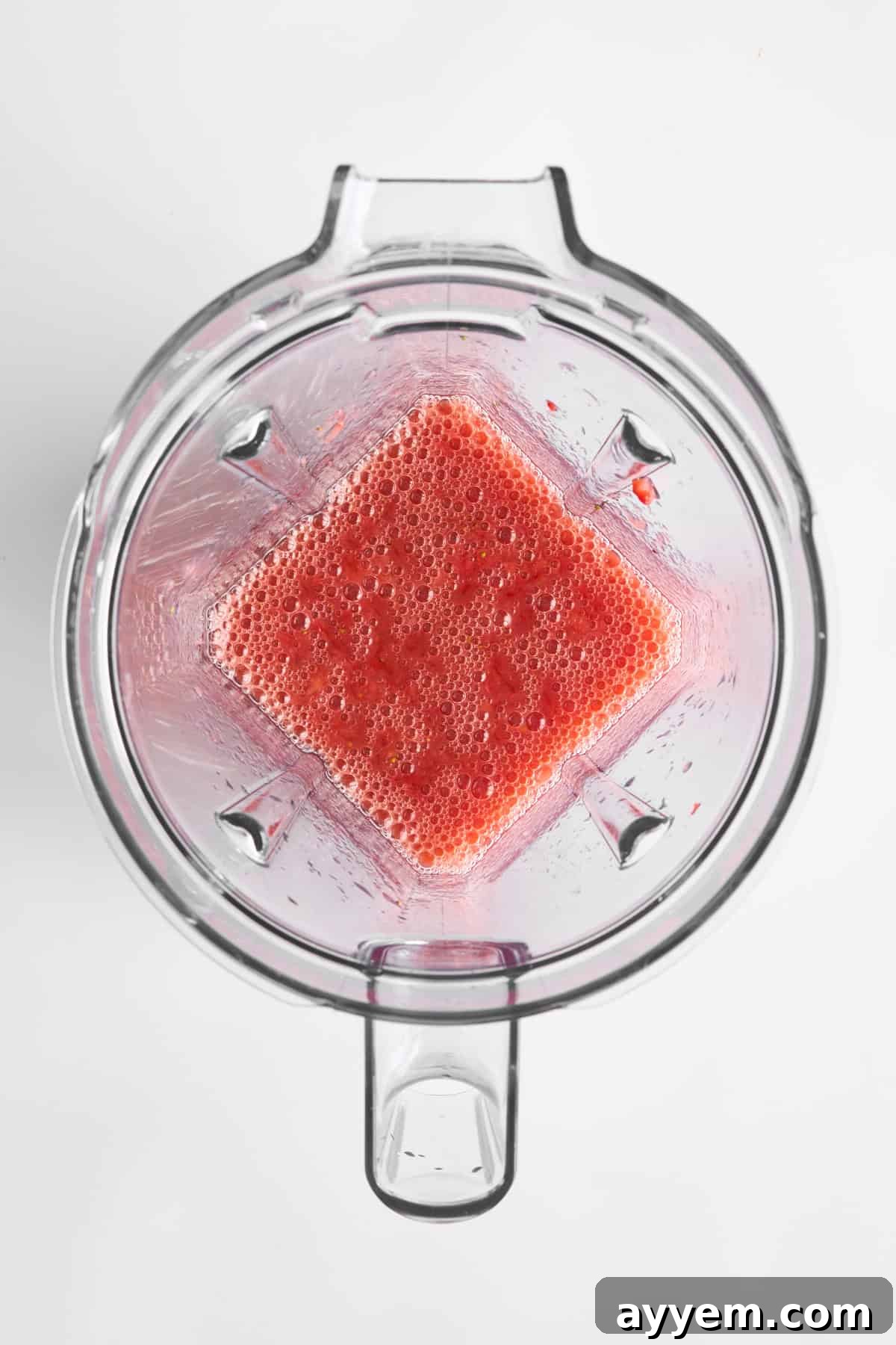 Fresh, ripe strawberries being pureed to a smooth consistency in a blender, capturing the vibrant red color.