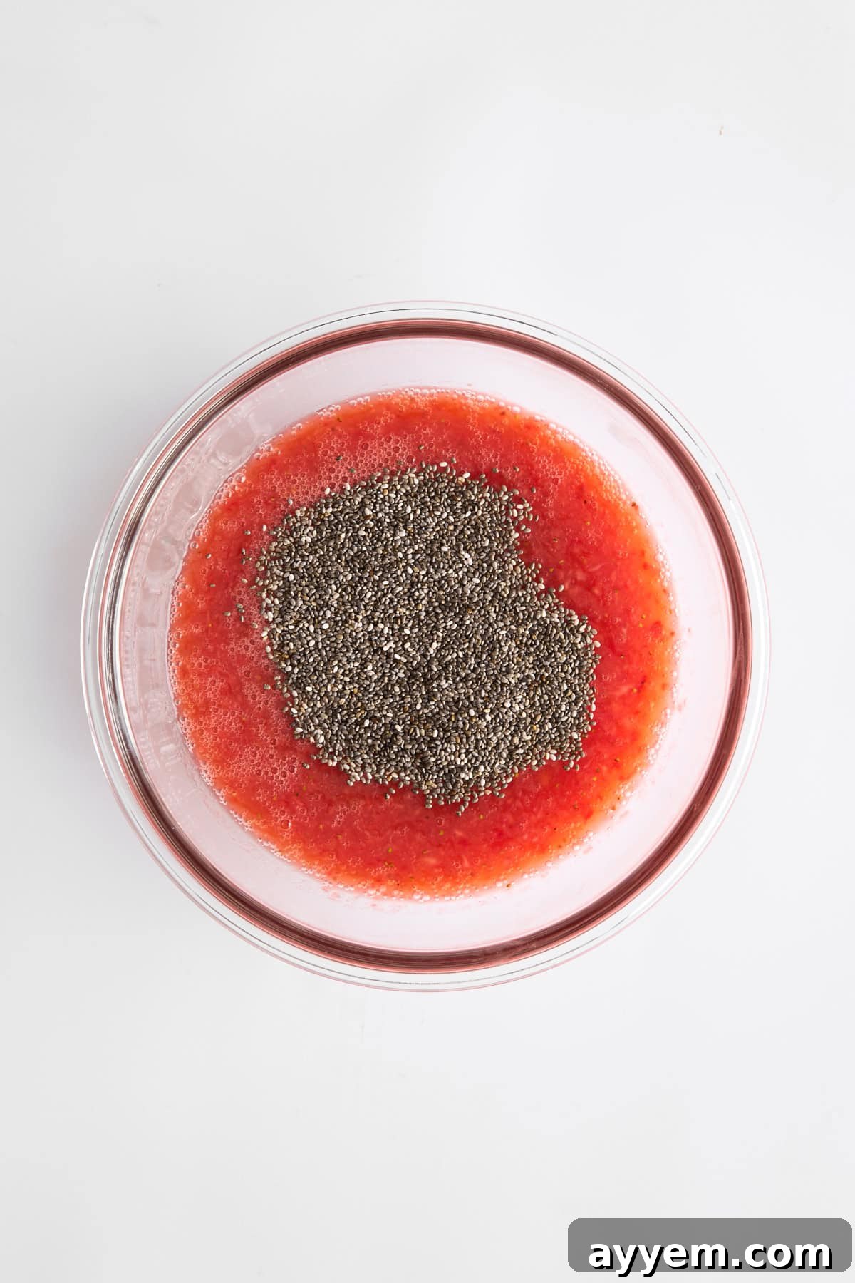 A bowl containing the beautiful strawberry puree, with chia seeds added and gently stirred in, highlighting the start of the pudding's transformation.