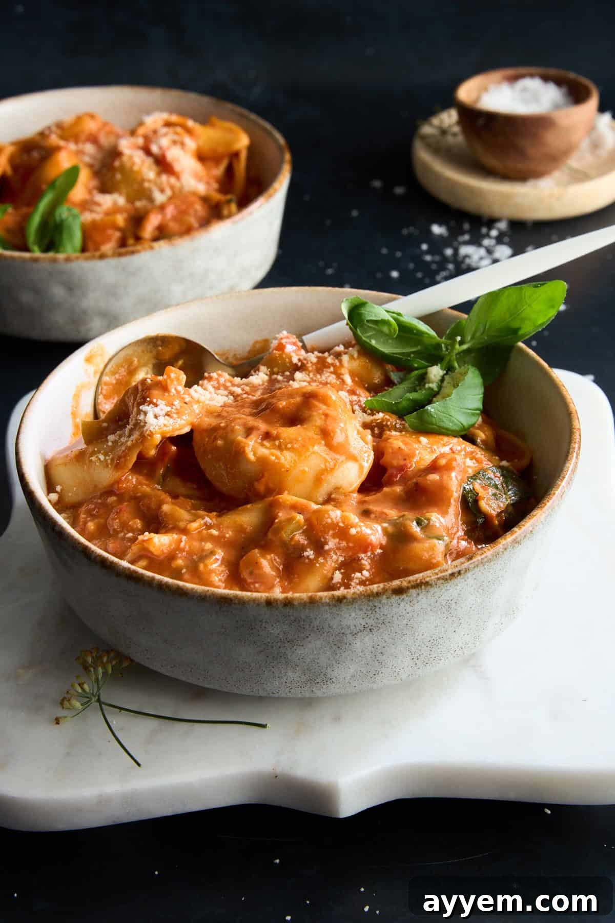 A serving of cheese tortellini soup with a spoon, highlighting its creamy texture and fresh ingredients.