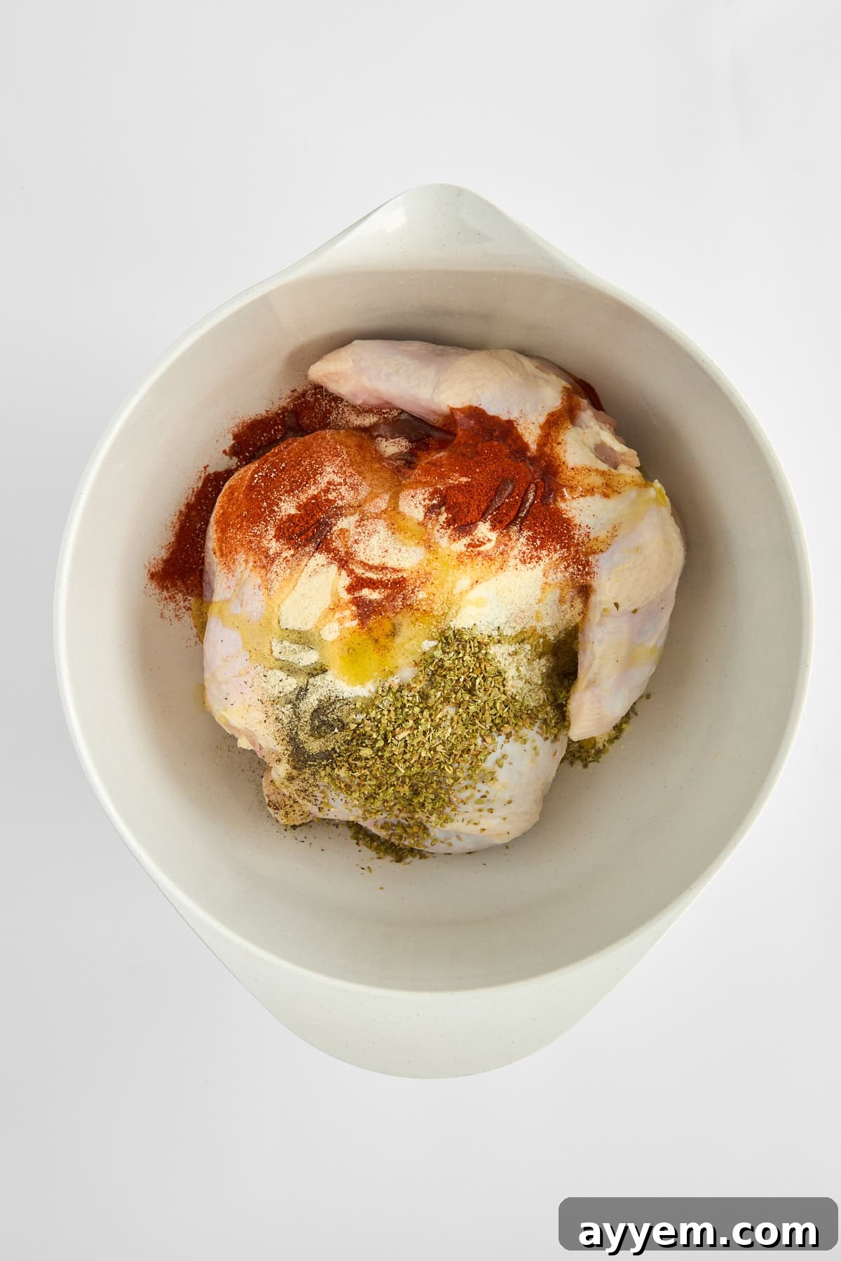 A raw whole chicken generously coated with seasoning.