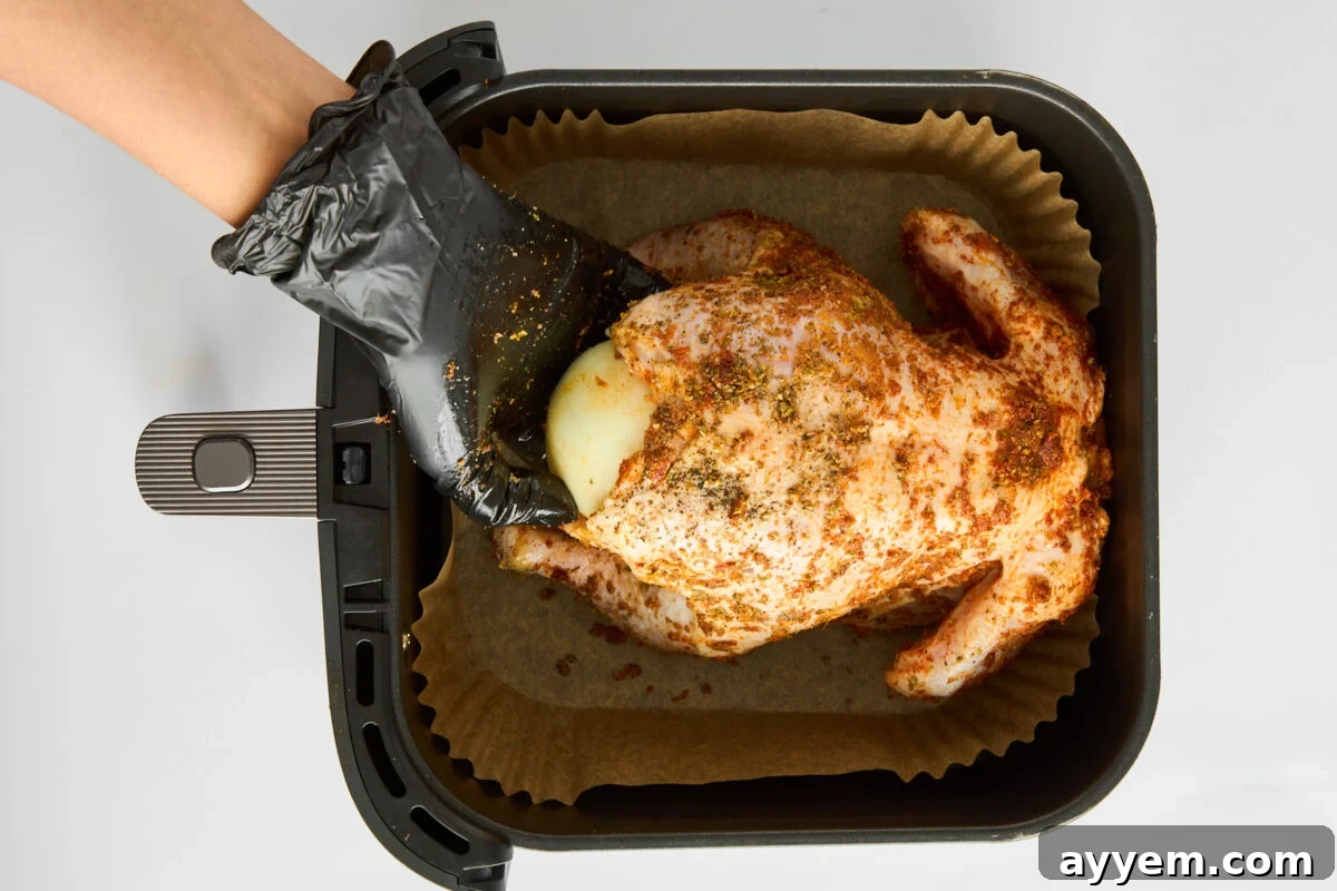 A hand stuffing a raw chicken with a halved onion.