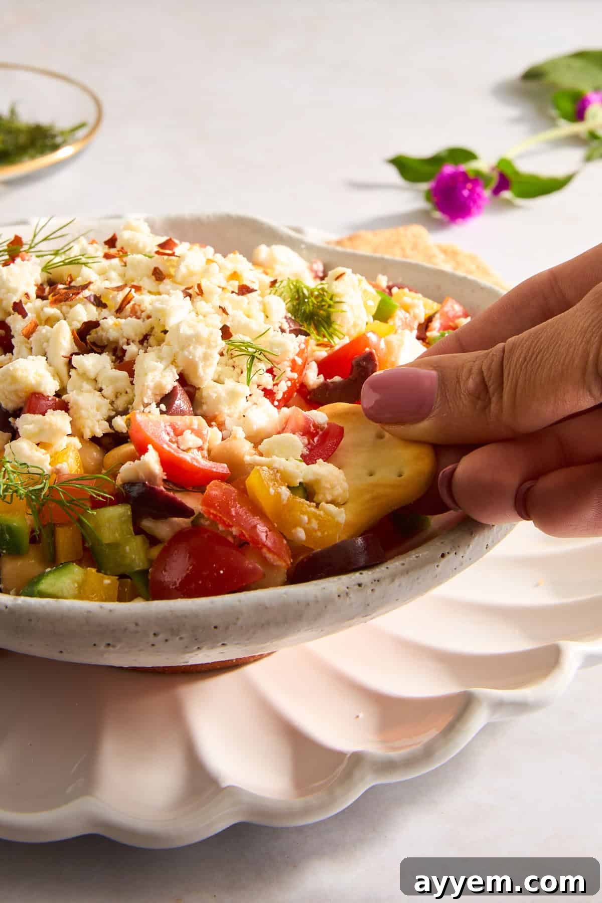 Whipped Mediterranean Feta 3 A close-up shot of a pita chip being generously dipped into a bowl of chunky Mediterranean feta dip, showcasing the vibrant colors and textures of the ingredients.