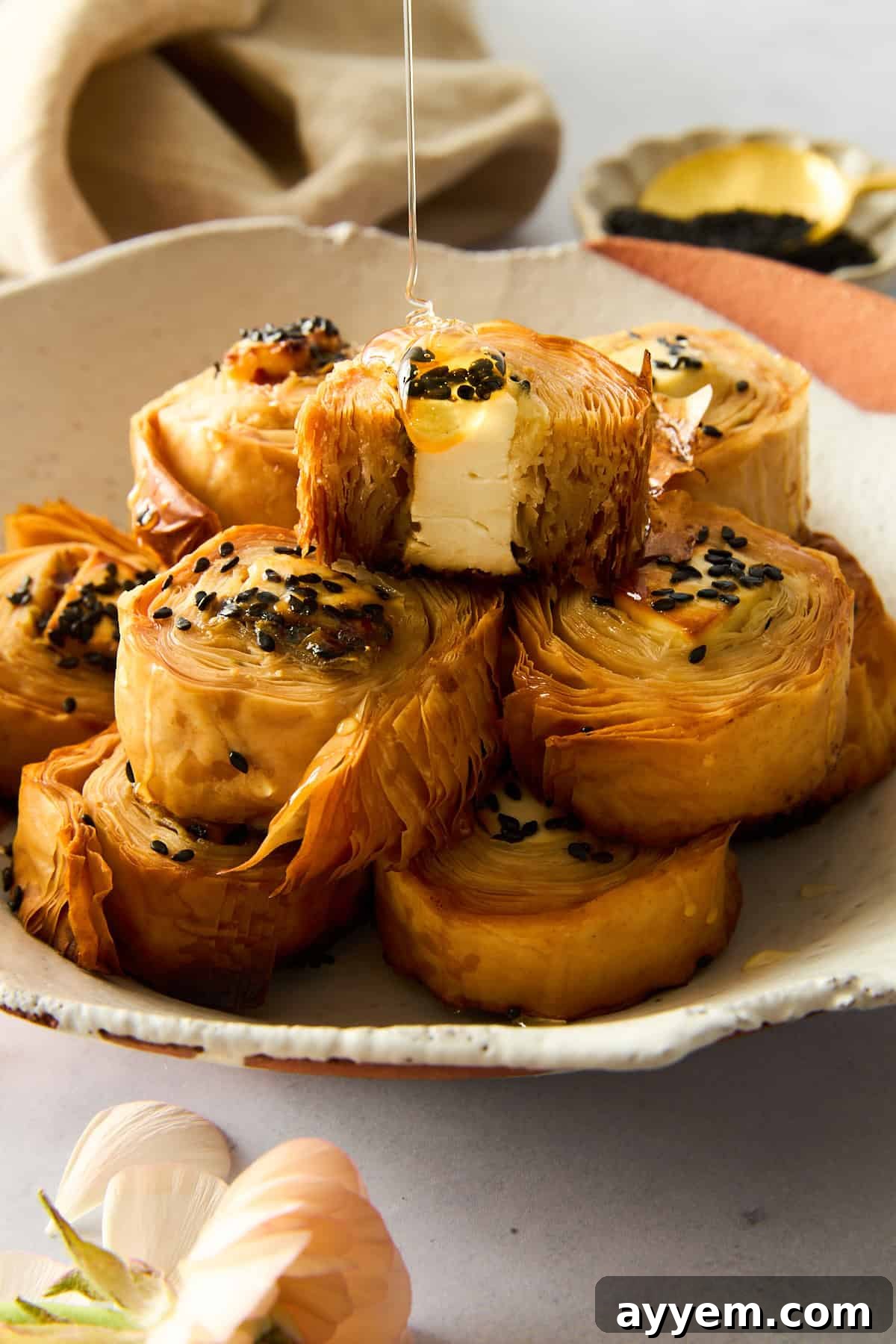 A plate of hot honey phyllo rolls with honey being drizzled on top, showcasing their crispy, golden texture.