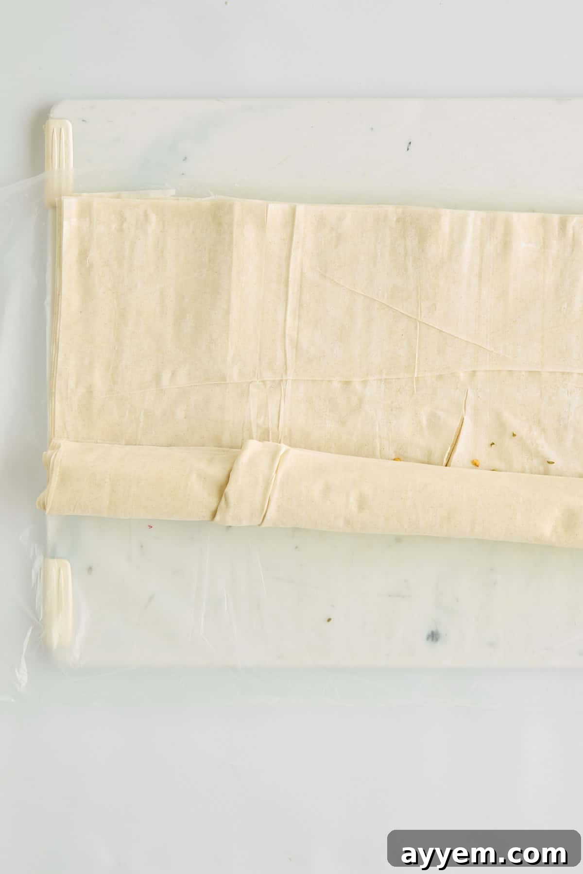 Phyllo dough being carefully rolled up with a savory feta and hot honey filling inside.