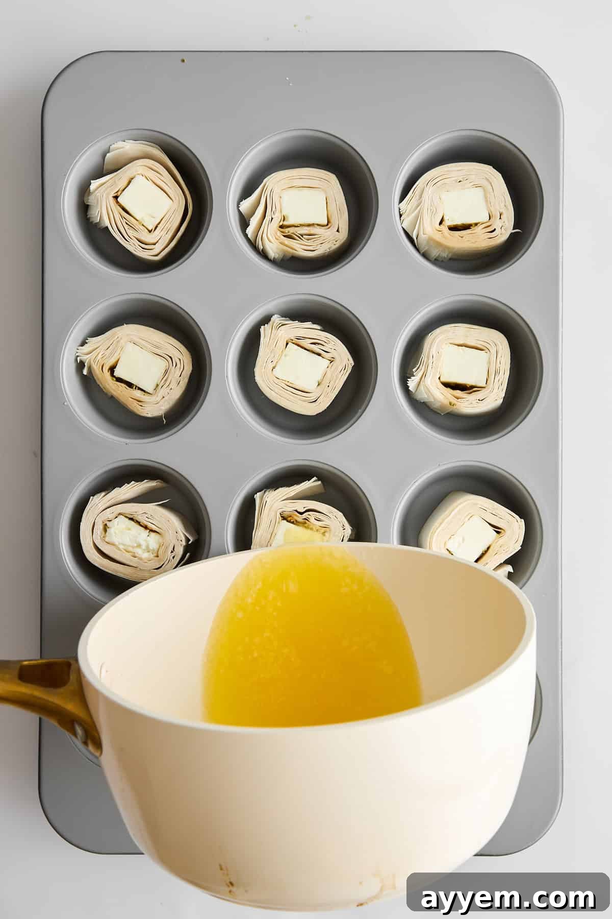 Feta phyllo rolls neatly arranged in a muffin pan and being brushed with melted butter.