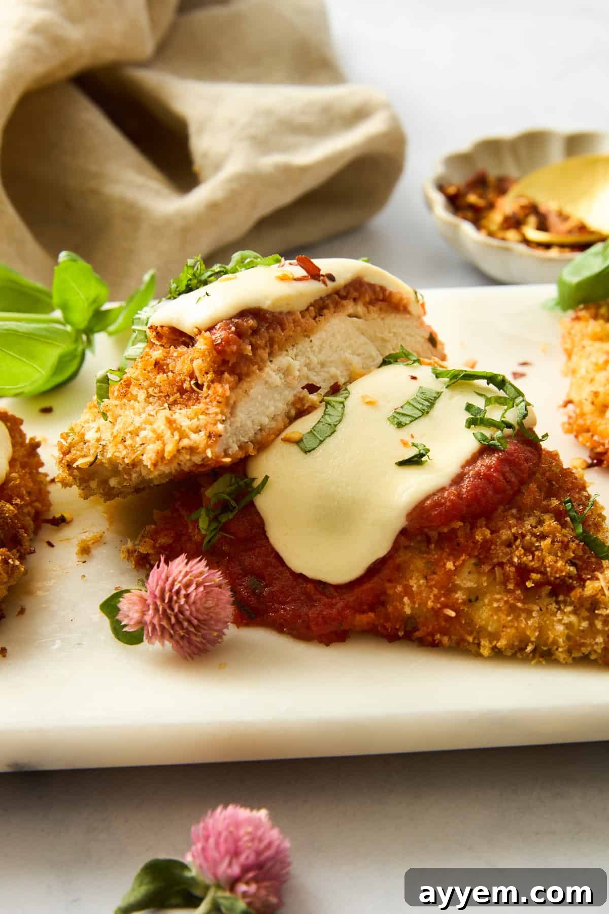 A perfectly sliced piece of baked chicken parmesan on a white plate, revealing the layers of crispy chicken, rich marinara, and melted mozzarella, garnished with fresh basil.