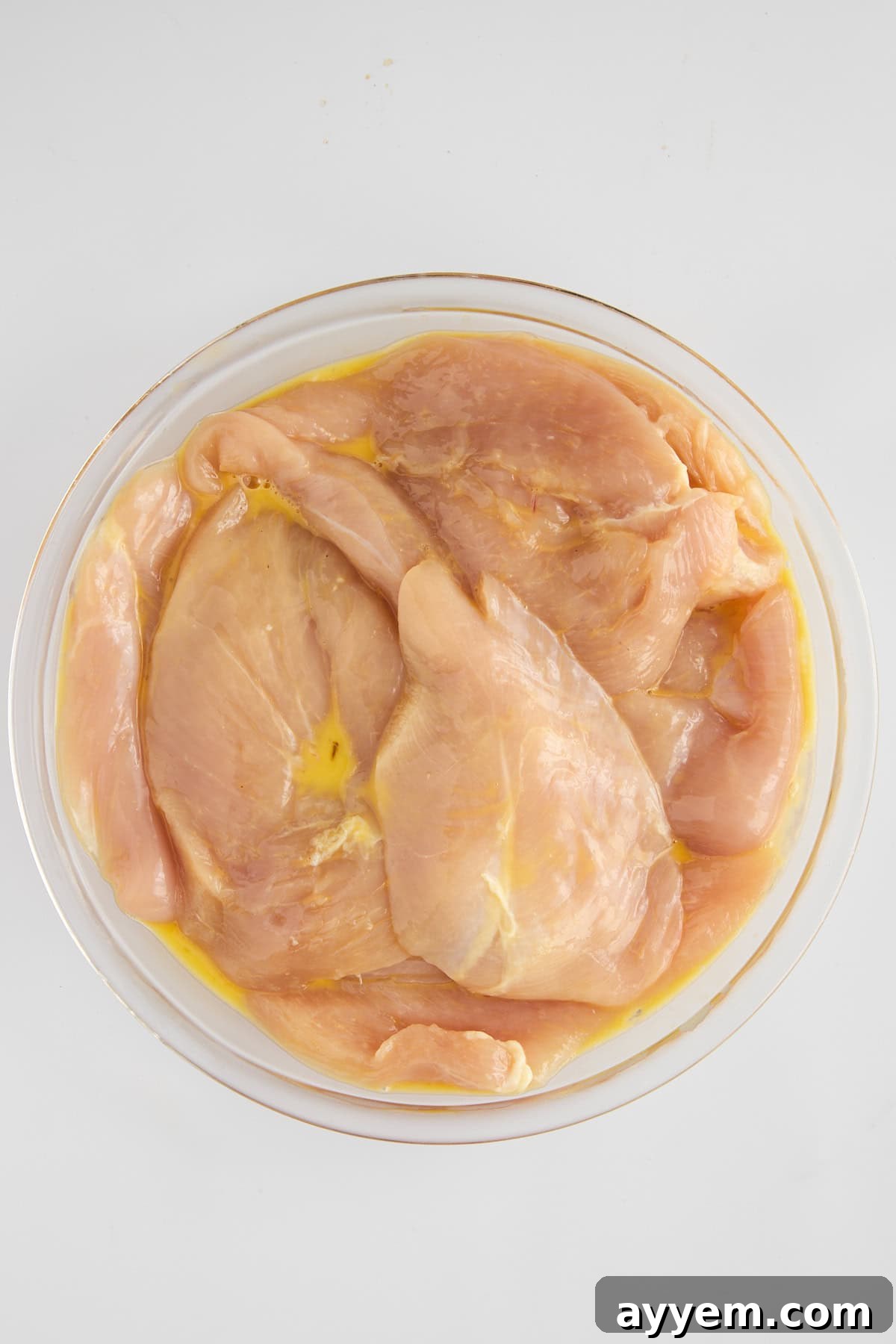 Raw chicken breast being dipped into a bowl of whisked egg wash, ensuring full coverage.