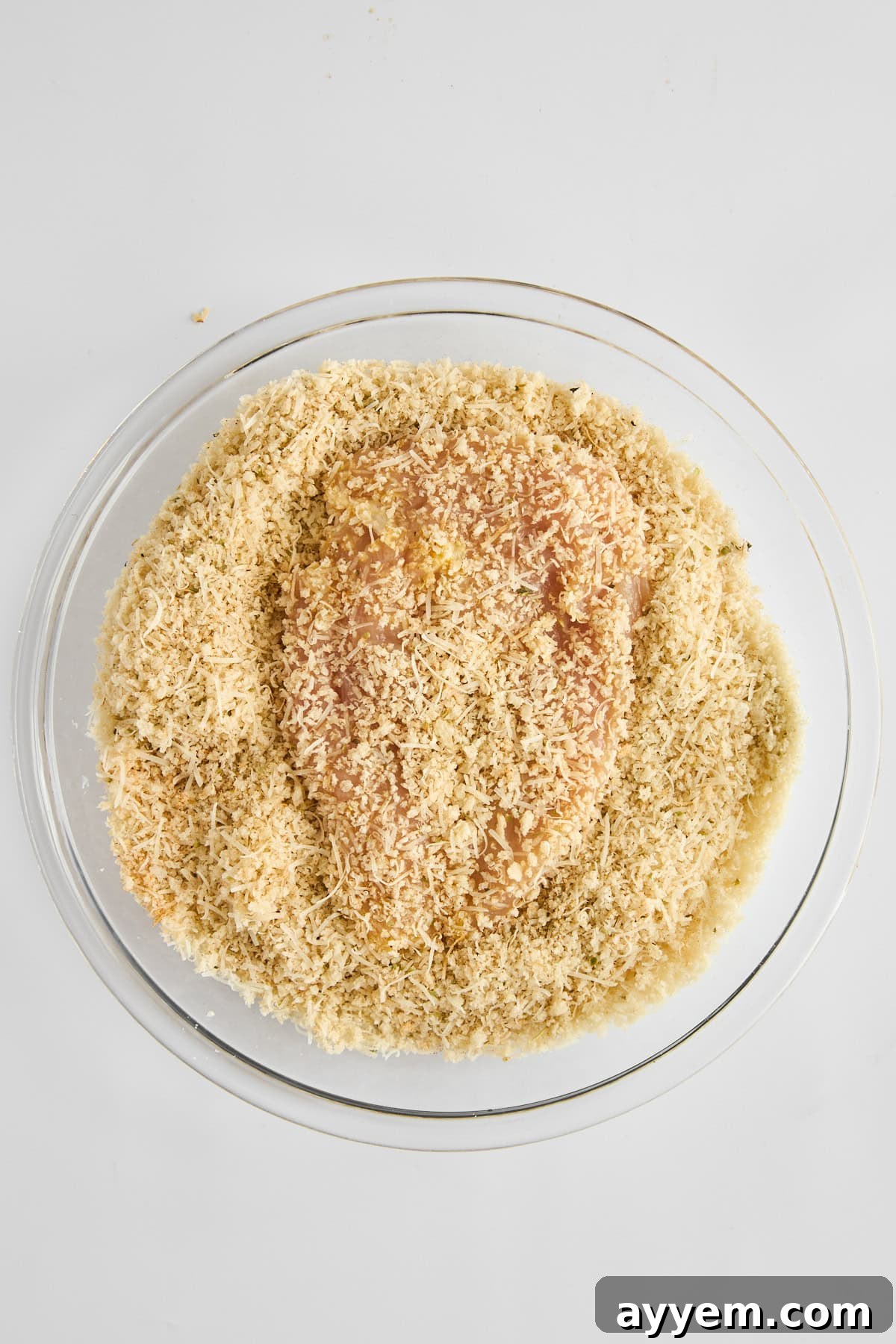 A single piece of raw chicken breast, fully and evenly coated in breadcrumbs, resting in a bowl.