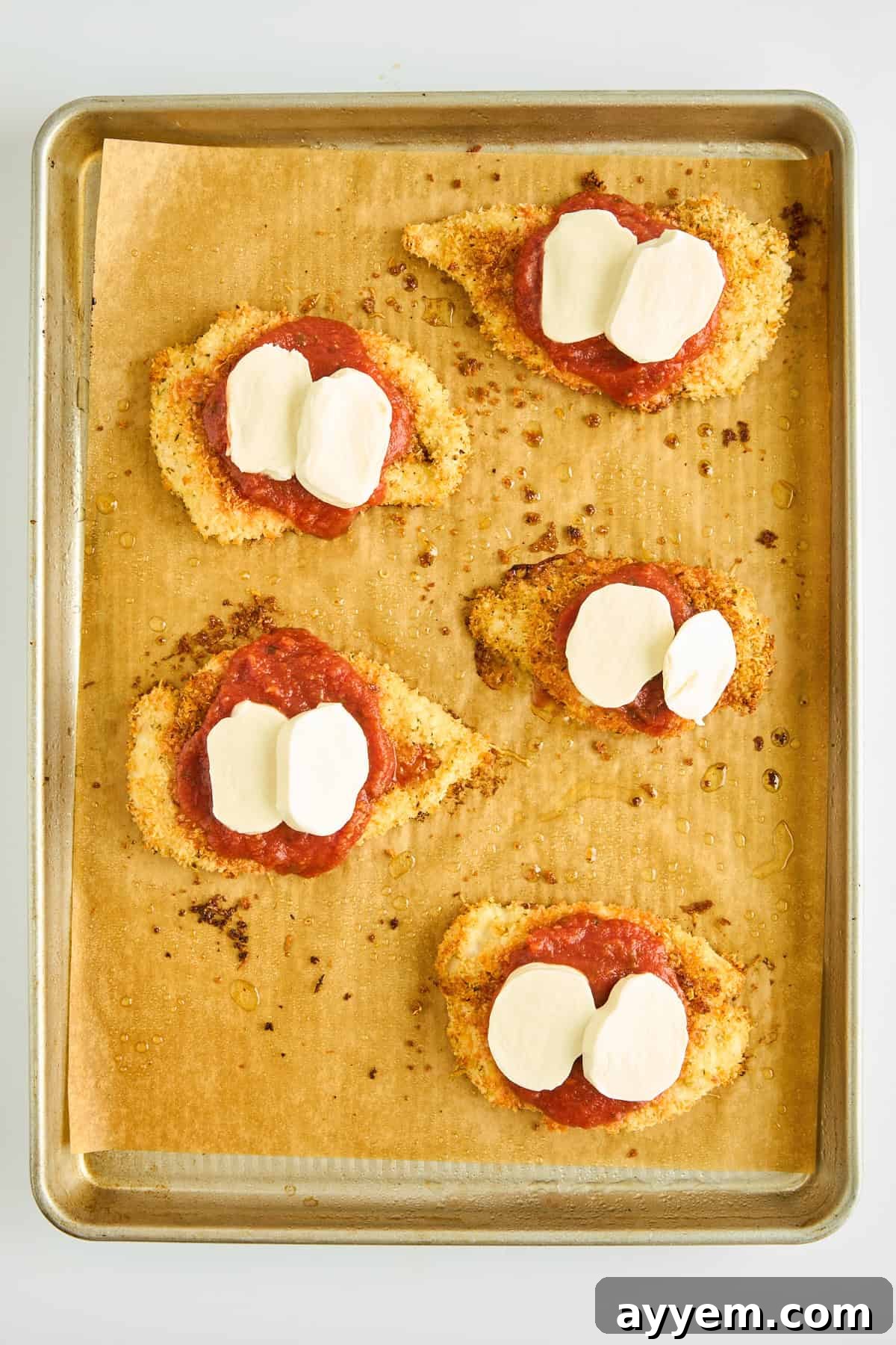 Unbaked chicken parmesan pieces, already topped with marinara and mozzarella, on a baking sheet.